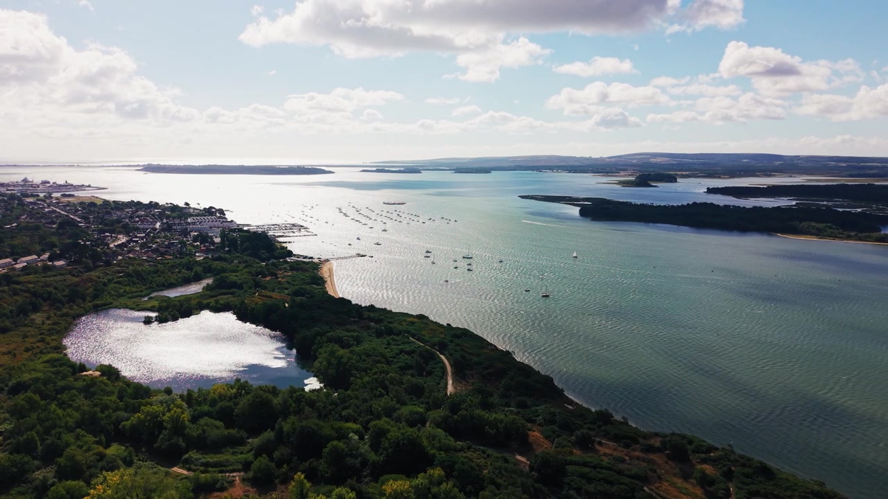Ampie riprese aeree che mostrano il porto di Poole nel Dorset, Inghilterra, con barche ormeggiate, isole boscose, zone umide costiere e la campagna circostante che si estende verso l'orizzonte. Aree residenziali.