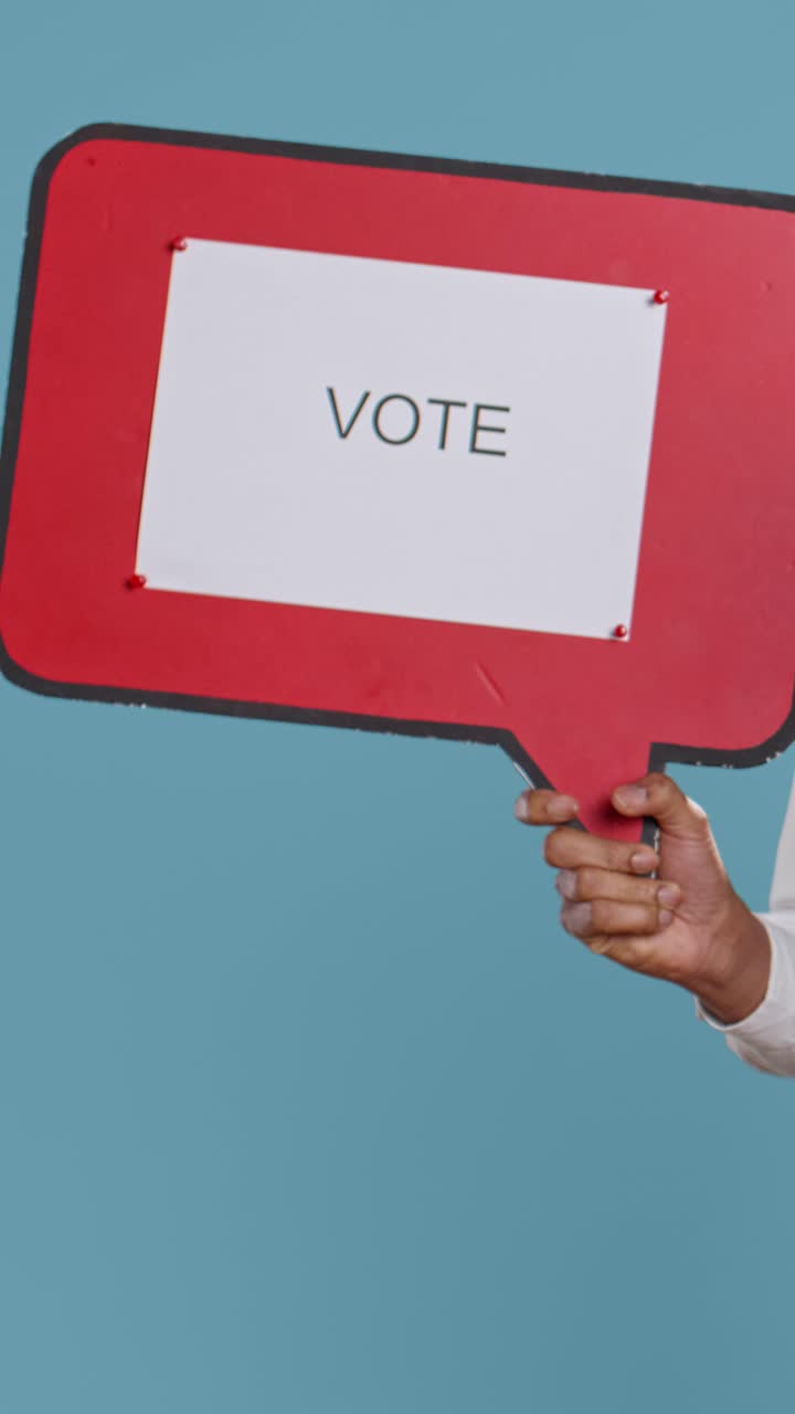 Person's Hand Holding Red Speech Bubble Sign with 'Vote' Message