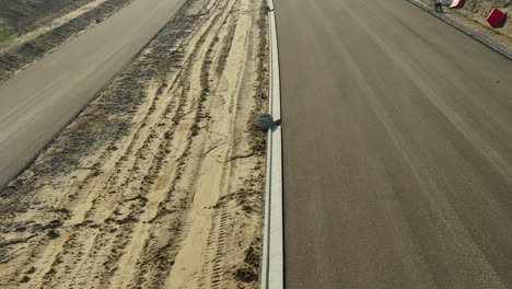 Cerrar-Vista-Aérea-De-Una-Carretera-Recién-Pavimentada-Junto-A-Un-Camino-De-Tierra