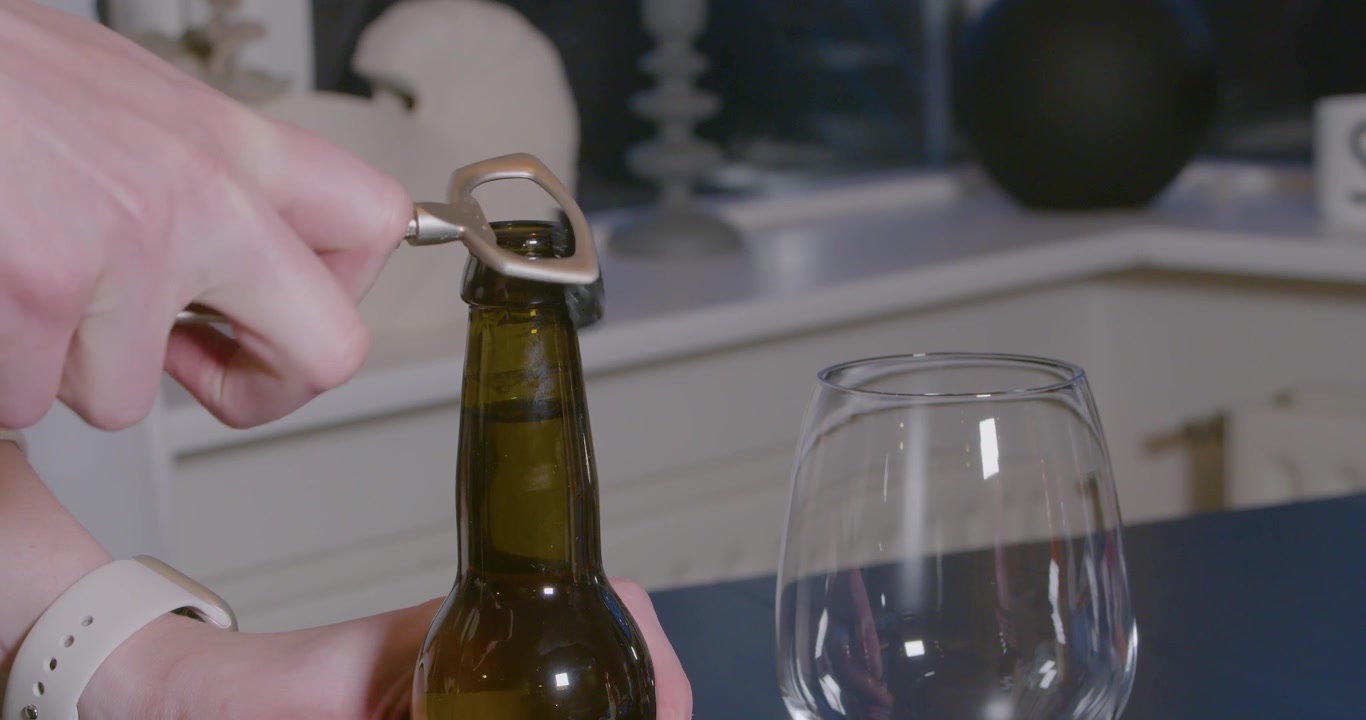 Abrindo uma garrafa de cerveja com um abridor de garrafas.