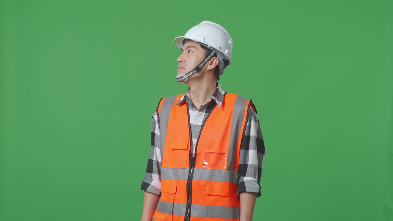 Asian Male Engineer With Safety Helmet Looking Around While Standing In The Green Screen Background Studio