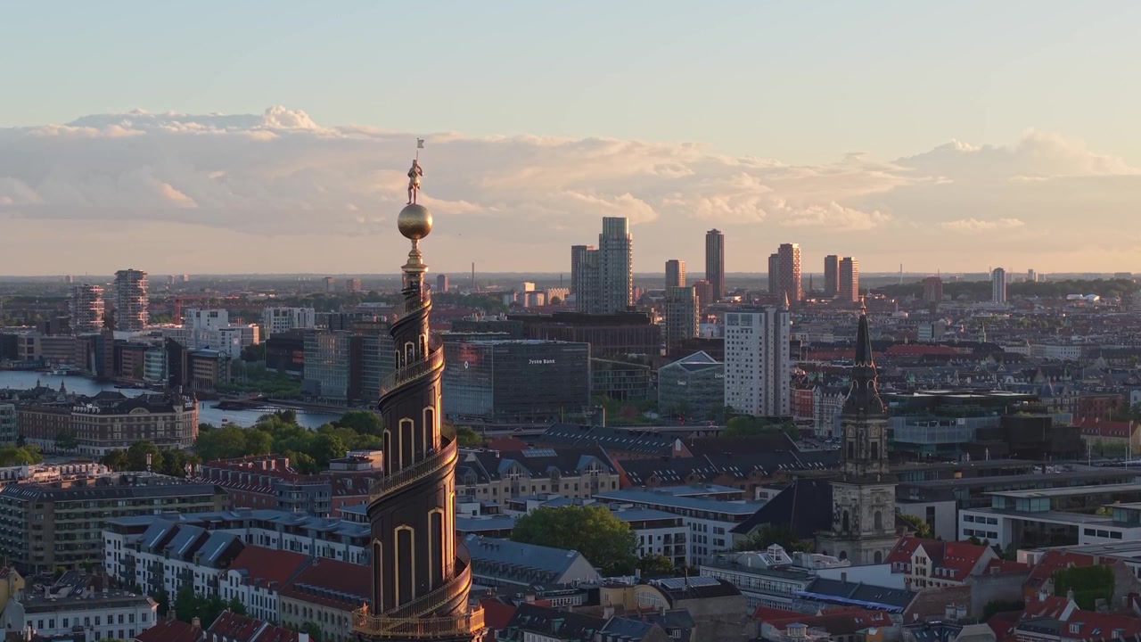 Riprese drone che salgono dietro il campanile della Chiesa del Nostro Salvatore (Vor Frelsers Kirke), rivelando gradualmente il paesaggio urbano di Copenaghen, l'architettura storica e lo skyline urbano dall'alto