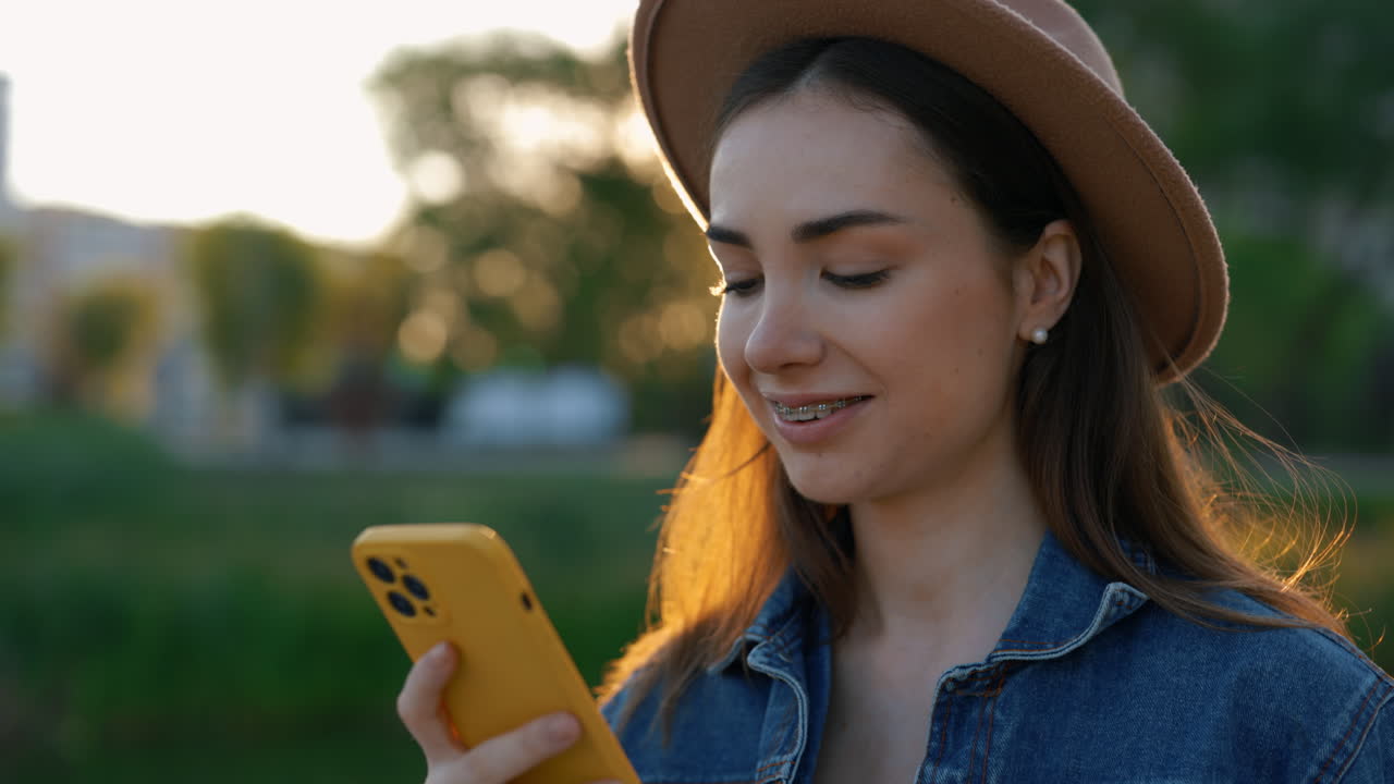 Woman using phone in park at sunset