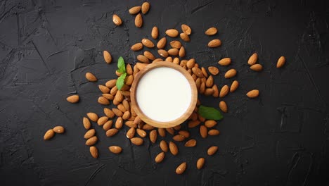 fresh almond milk in wooden bowl and almonds on black stone background