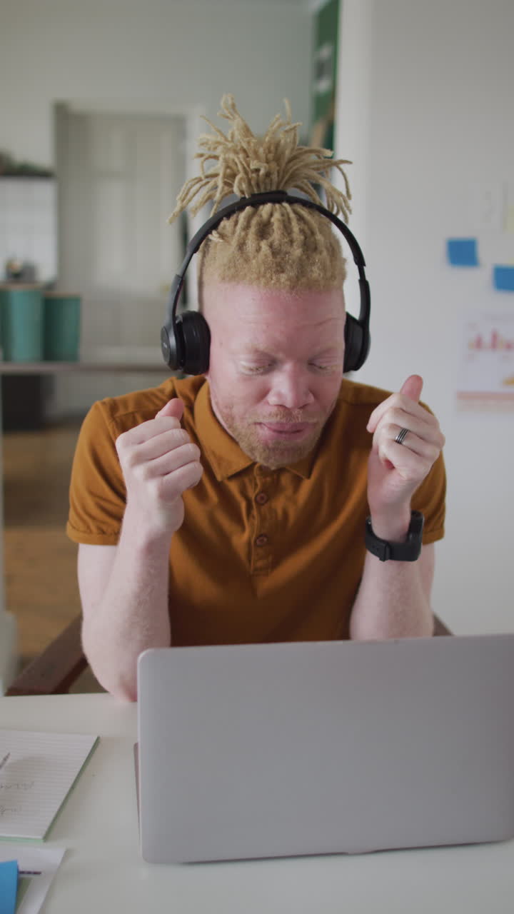 Toma vertical de un hombre albino haciendo una videollamada en su portátil, usando auriculares