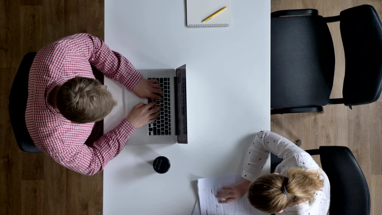 Telecamera che si muove sopra uomini d'affari che lavorano e siedono al tavolo in un ufficio moderno, ripresa dall'alto
