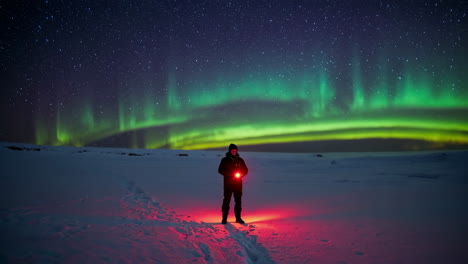 lone person with red light under vibrant aurora borealis in snowy landscape