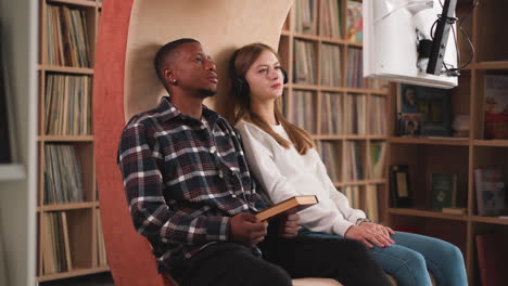 una pareja ve un video informativo en la biblioteca. un chico afroamericano y una mujer blanca estudiantes amigos estudian material visual a través de la televisión en el almacén de libros de la universidad. instalación de educación
