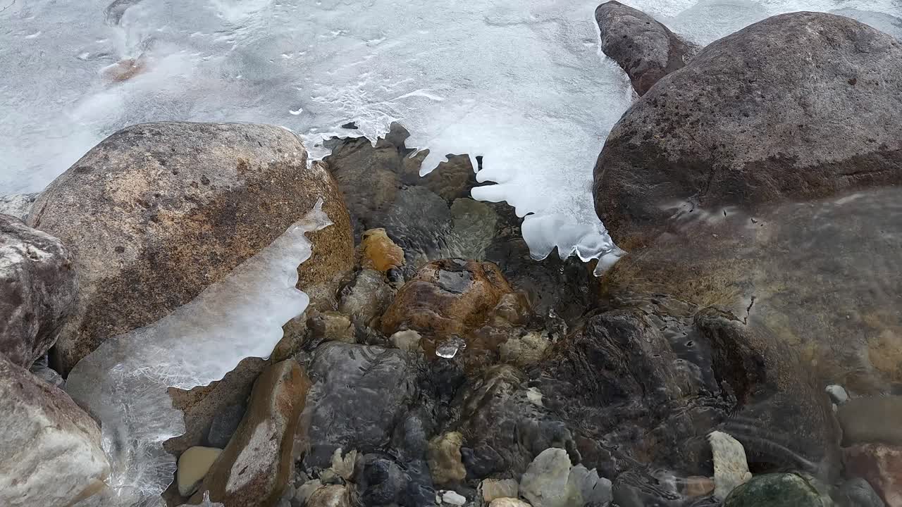 Kevät vuoristopurolla. Vettä virtaa jään alla pitkin vuoristopuroa, kuvattuna lähikuvana.