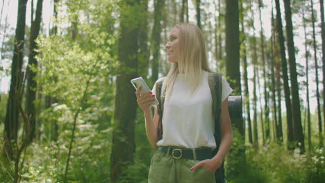 Una-Mujer-Atractiva-Se-Relaja-En-El-Bosque-Y-Usa-Un-Teléfono-Inteligente-Al-Aire-Libre.-Mujer-Caminando-Por-El-Bosque-Y-Escribiendo-Mensajes-En-Un-Teléfono-Inteligente.-Excursionista-Solitaria-Usando-Un-Teléfono-Inteligente.