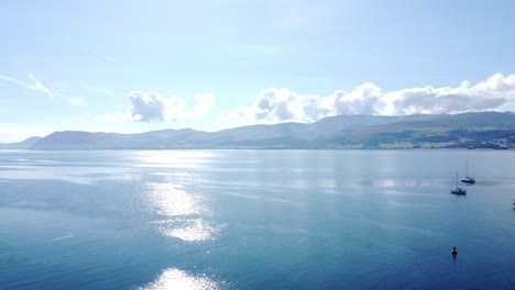 Snowdonia-clear-mountain-range-aerial-view-panning-across-sunny-calm-Welsh-shimmering-seascape