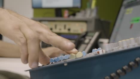 Anonymous audio engineer adjusting sound mixer knobs in recording studio, slow motion