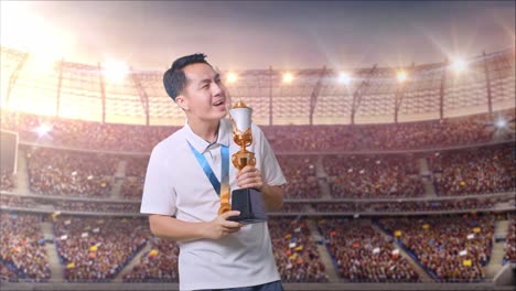 금메달을 가진 아시아인 남자가 금 트로피에서 노래하며 경기장에서 첫 번째 우승자로 우승을 축하하고 있습니다.