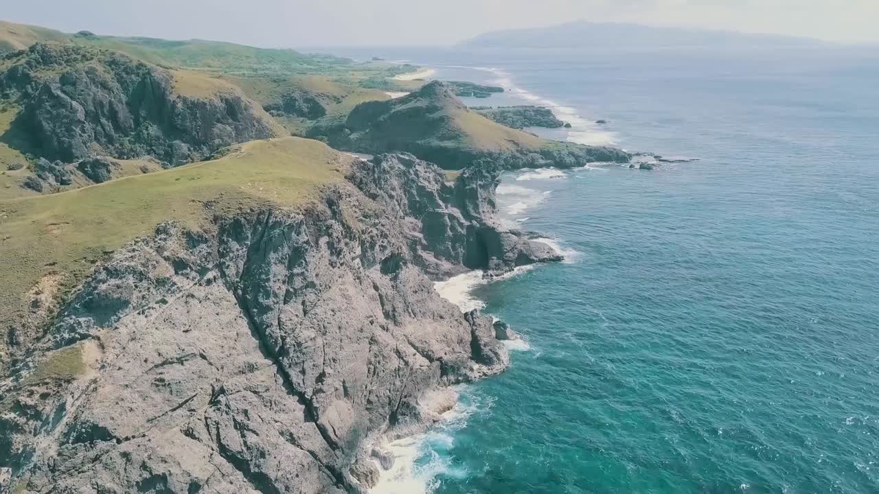 Cinematic aerial drone video of splashing ocean waves into a scenic mountains of Sabtang, Batanes in the Philippines.