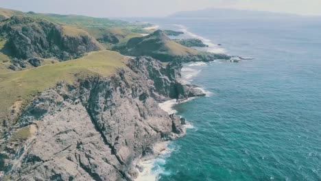 cinematic aerial drone video of splashing ocean waves into a scenic mountains of sabtang, batanes in the philippines.