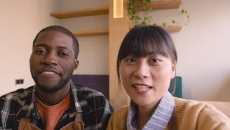 waiter and waitress taking a selfie video and talking to camera while sitting at table in coffee shop 1