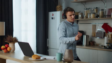 Man-dancing-kitchen-headphones-listening-music-on-laptop.-Guy-singing-melody.