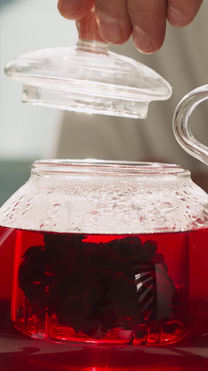 Man carefully puts cap on teapot with brewing tea in kitchen. Process of brewing hibiscus healthy tea according to traditions. Morning tea-time ritual