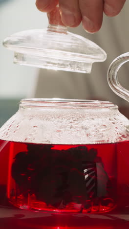 el hombre pone cuidadosamente la tapa de la tetera con el té de cerveza en la cocina. proceso de elaboración del té saludable de hibisco de acuerdo con las tradiciones. ritual de la hora del té por la mañana