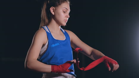 middling plan beautiful athletic boxer in blue clothes reels red bandages on the hands of a female fighter. steadicam shot