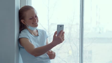 woman video chatting at a window, hospital gown, mask