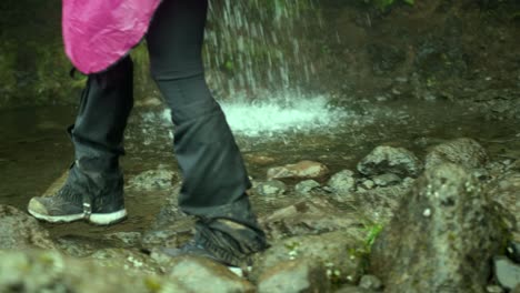 excursionista caminando por las rocas más allá de una cascada y recogiendo agua en su palma