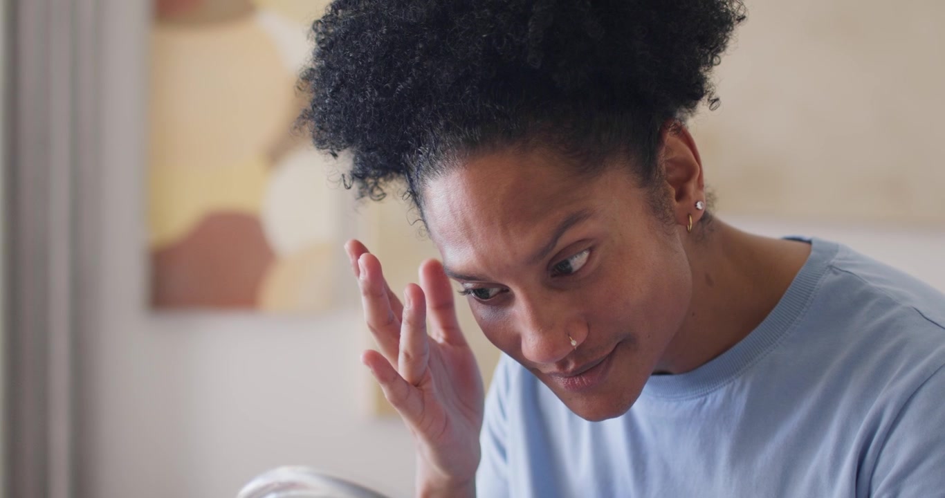 Adult African American female raising right hand, checking eyebrow for spot using compact at vanity