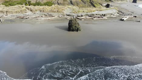 drone flies backwards away from person standing on a sea stack on the beach