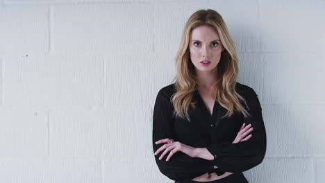 fashion portrait of serious young woman standing against white studio wall