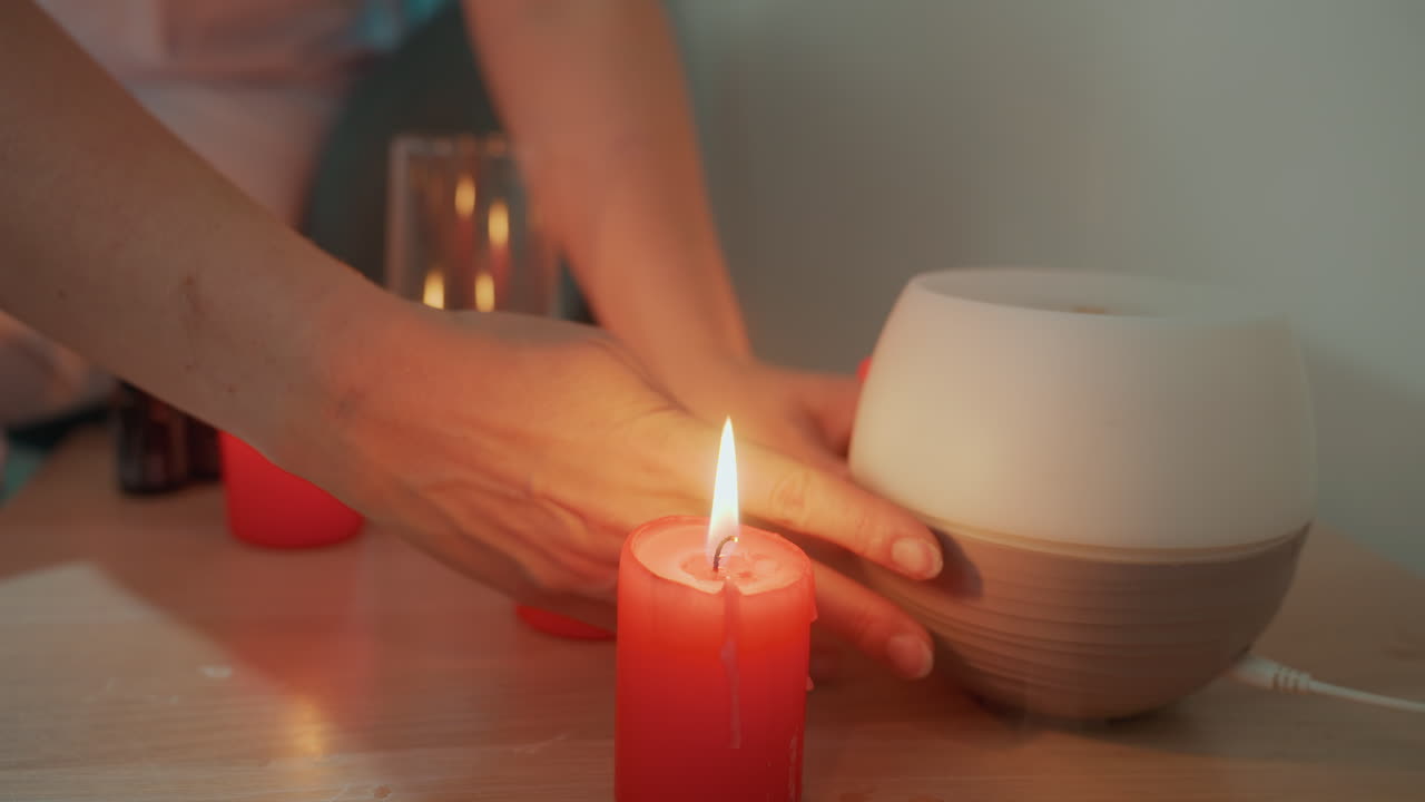 Candle diffuser with gentle light promotes relaxation and tranquility at home. Caucasian woman activates smart diffuser emitting soft yellow illumination for peaceful relaxation environment