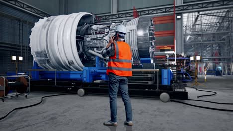 full body back view of asian male engineer with safety helmet talking on smartphone while standing with airplane engine maintenance conducted, analytics checking the turbine