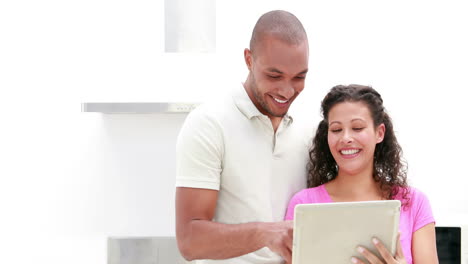 Smiling-couple-discussing-over-a-tablet-in-the-kitchen