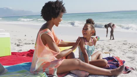 familia afroamericana sonriente usando crema solar en una playa soleada