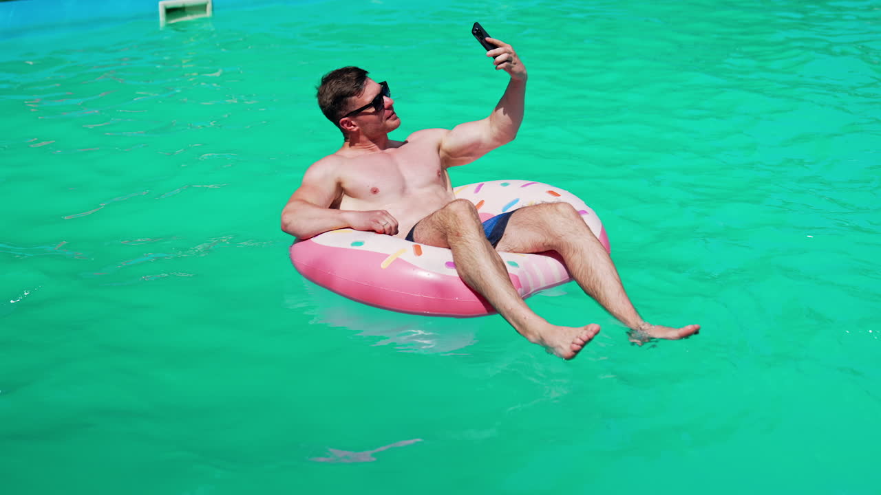 Man taking a selfie in a pool with a donut float