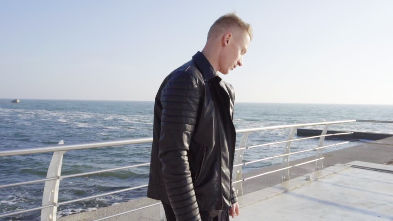 Young man in a leather jacket skating on his longboard by the sea