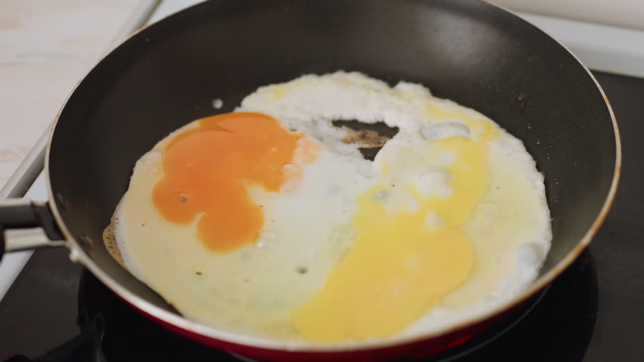 Tampilan close up telur yang digoreng di wajan di atas kompor panas dengan kuning telur yang menggelembung dan putih telur yang menyebar di permukaan saat memasak sarapan di dapur rumah yang menunjukkan detail mendesis dari persiapan makanan segar