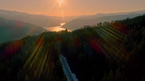 aerial drone shot over incredibly beautiful snow covered road over mountainous landscape in norway with sun setting in the background