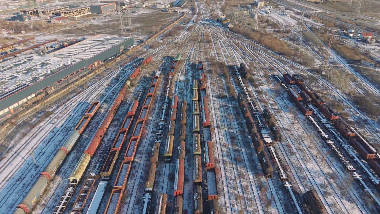 Schnee bedeckter Güterbahnhof am Rande von Iași, Rumänien. Parallele Linien von geparkten Waggons und Lokomotiven aus der Drohnenperspektive sichtbar, klares Winterlicht