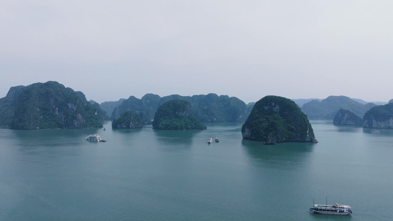 Boats cruising between limestone islands on a misty day in Ha Long Bay, Vietnam