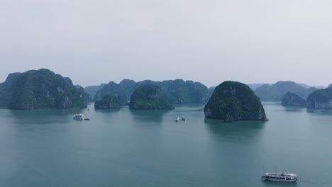 boats cruising between limestone islands on a misty day in ha long bay, vietnam