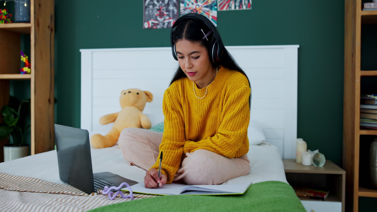 Teenage girl studying on bed with laptop and headphones
