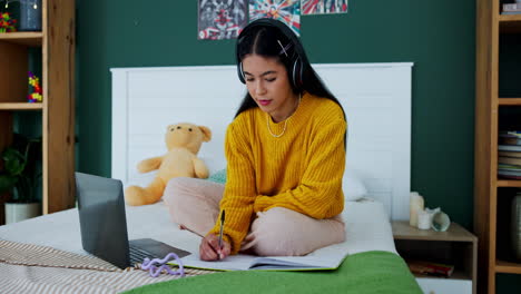 teenage girl studying on bed with laptop and headphones