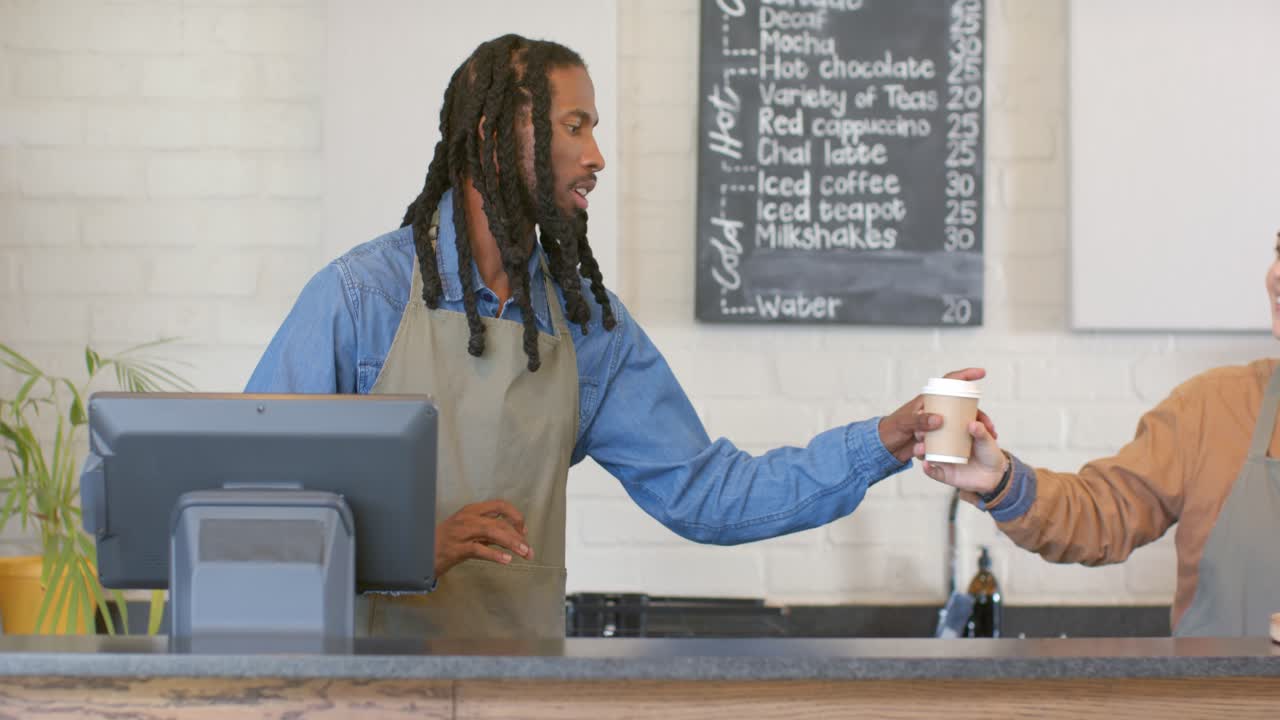 Barista afro-americano digitando no terminal, pegando um copo e servindo um cliente no balcão de um café