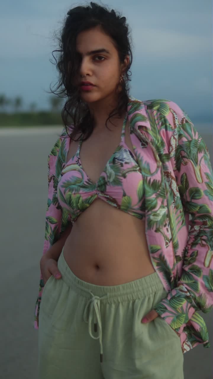 Woman in tropical bikini top walks along beach at sunset with tousled hair and relaxed vibe, vertical shot
