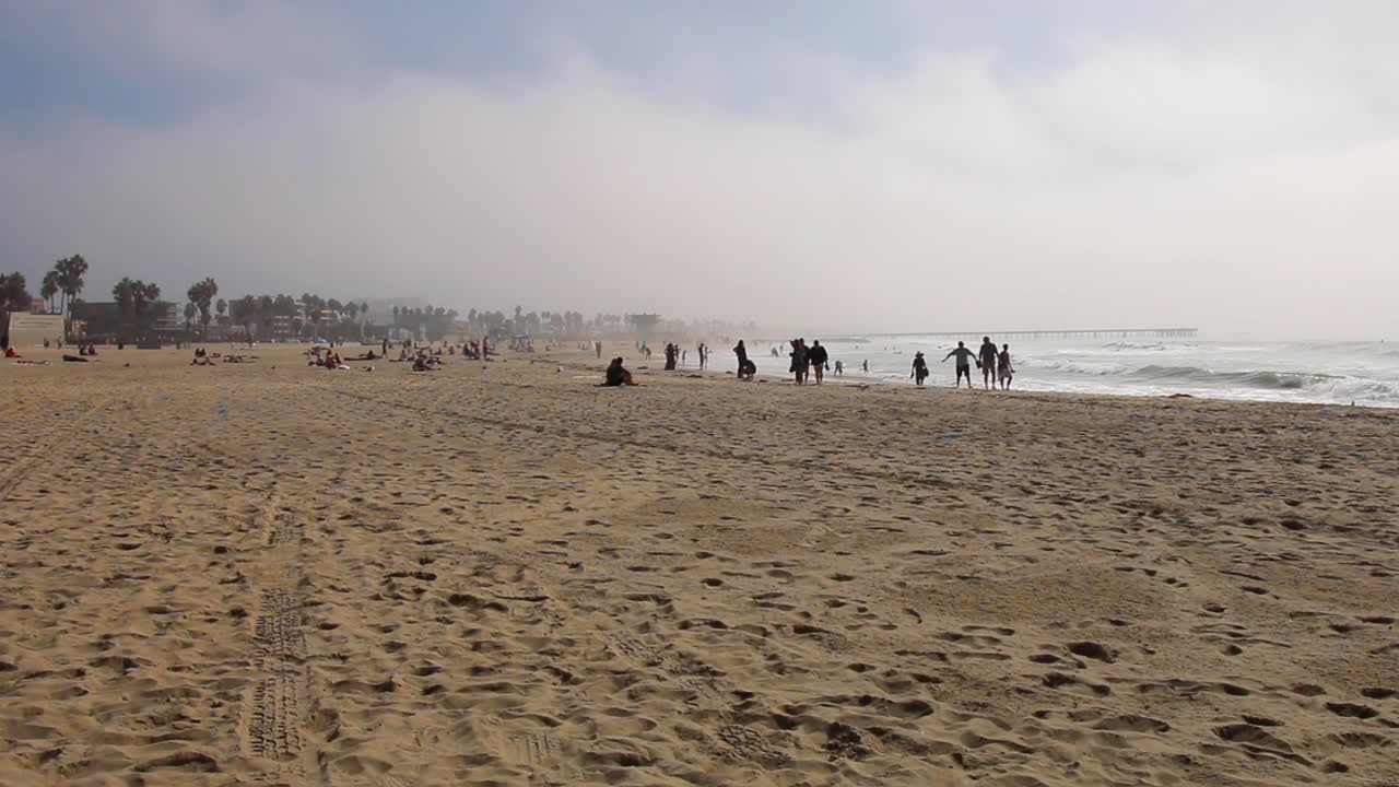 파도가 튀는 베니스 해변을 따라 걷는 사람들