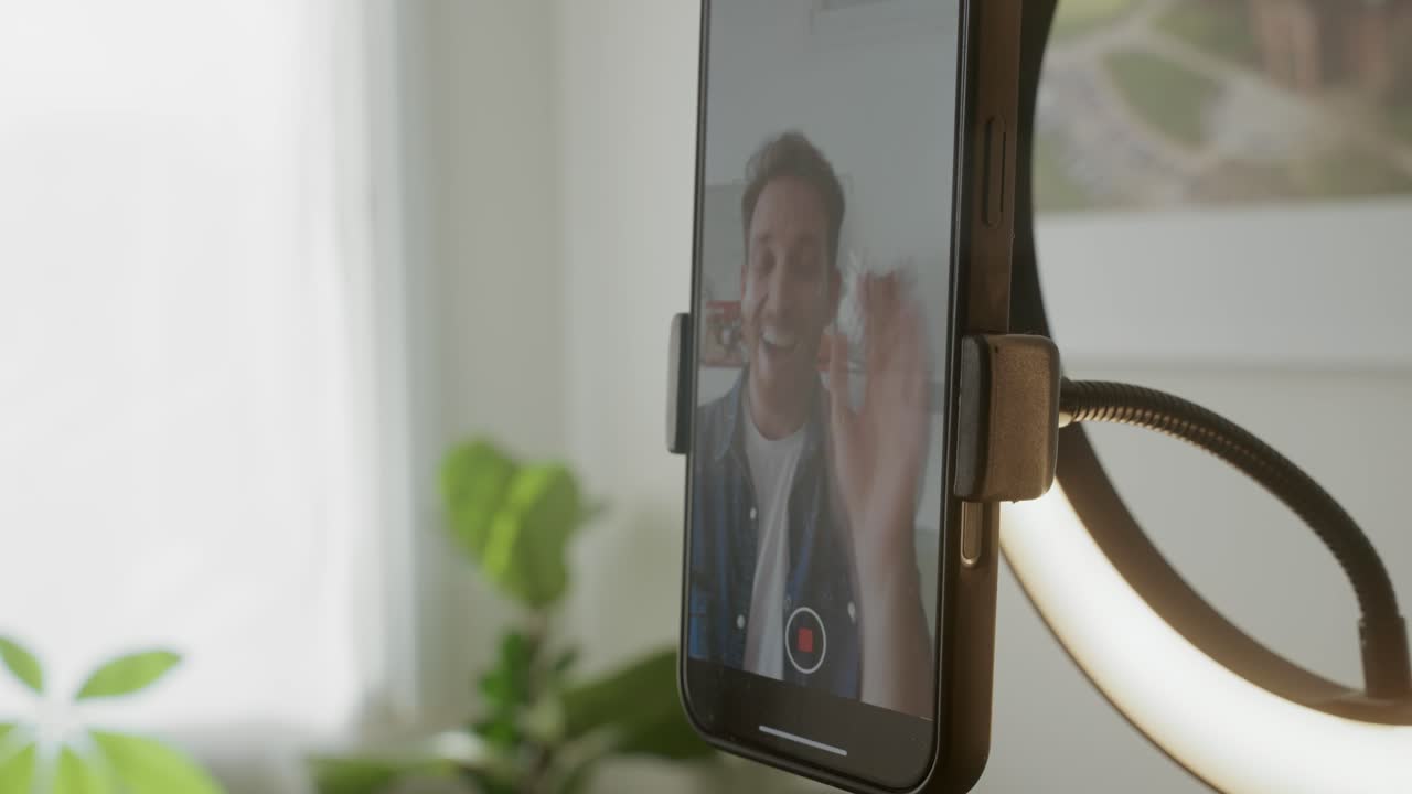 Close up on phone man pressing record button on screen filming vertical video talking. Social media ad or reel from content creator or influencer. Selfie mode. Mobile camera on ring light stand holder