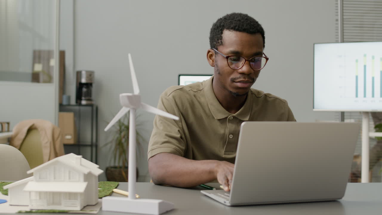 Businessman Using Laptop Sitting At Table With Windmill Model In The Office 4
