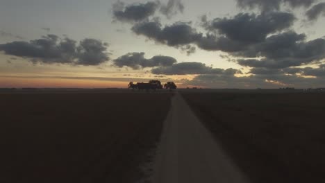 Flug-über-Grasfeld-Und-Feldweg-In-Richtung-Einer-Baumgruppe-Auf-Dem-Südlichen-Bauernhof-Bei-Sonnenaufgang