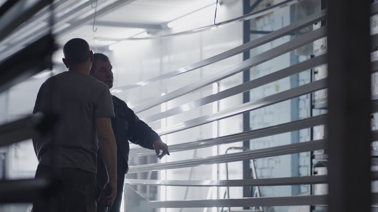 dos pintores masculinos que trabajan en la fábrica preparan elementos metálicos de acero para pintar fijándolos en suspensiones. pintar piezas en la sala de producción. filmar en cámara lenta.