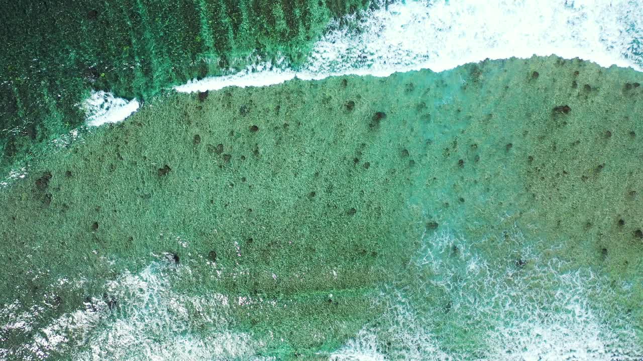 Peaceful sea scenery with white waves covering calm turquoise lagoon water, rocks and corals on shore of tropical island in Antigua